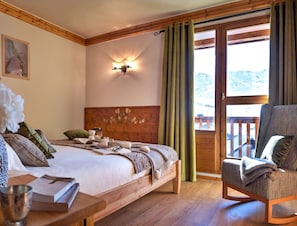 Ein Schlafzimmer mit einem Holzkopfteil, einem Bett mit Kissen und Decke, einem Nachttisch mit Buch und Glas sowie einem Sessel mit Decke.
