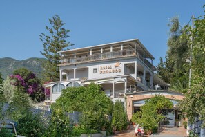 Un hôtel appelé « Hôtel Pégase », avec une structure à deux étages, des balcons, et entouré d’une végétation luxuriante et de montagnes.