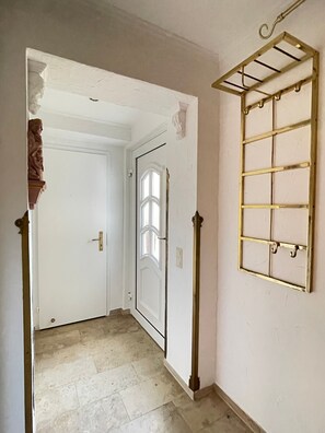 Ein Flur mit einer weißen Tür, einem Fenster mit dekorativem Rahmen und einem Metallregal an der Wand.