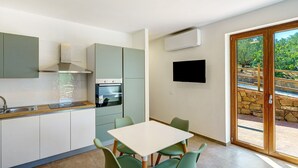 A modern kitchen with a dining area, built-in oven, and a TV mounted on the wall. - Apartment 3 - Leucosia with Sea View, Private Terrace, and Air Conditioning (Casal Velino)