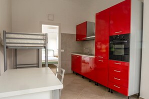 Uma cozinha com armários vermelhos, uma mesa branca e uma cama beliche.