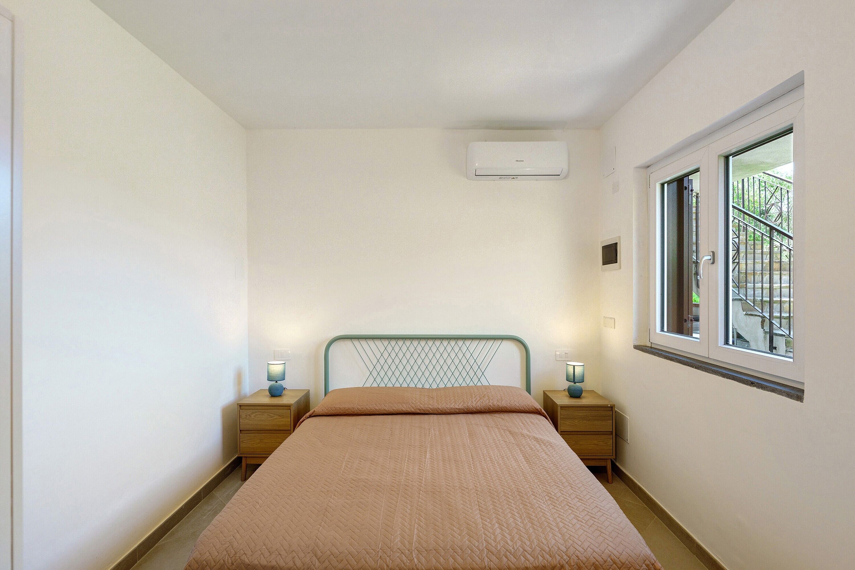 Ein Schlafzimmer mit einem Bett, zwei Nachttischen, einem Fenster und einer Klimaanlage.