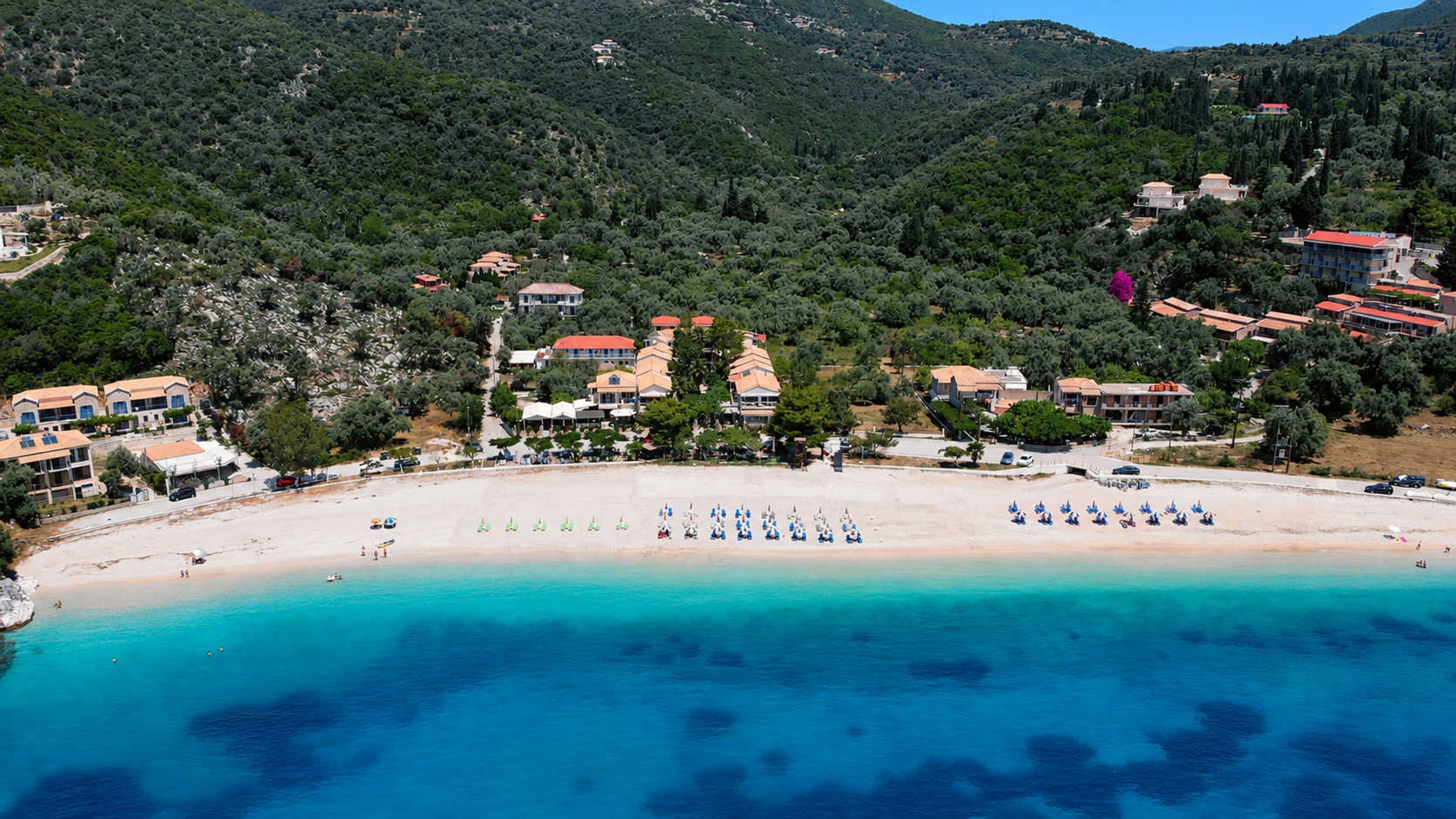 A coastal resort with beach, villas, and mountainous backdrop.