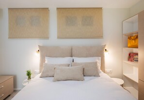 Une chambre à coucher bien rangée, avec un lit, des tables de chevet, une commode, une étagère fixée au mur et une plante en pot.
