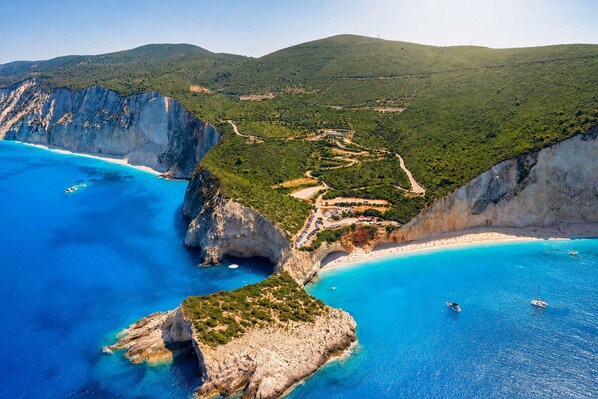 Paesaggio costiero con scogliere, una spiaggia e imbarcazioni.