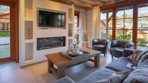 Ein Wohnzimmer mit Kamin, Fernseher, Sofa und Blick ins Freie.