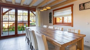Ein Essbereich mit Holztisch, weißen Stühlen, großen Fenstern und Holzboden.