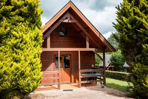 Eine Holzhütte mit Satteldach, einer Haustür und einer kleinen Veranda mit einer Bank.