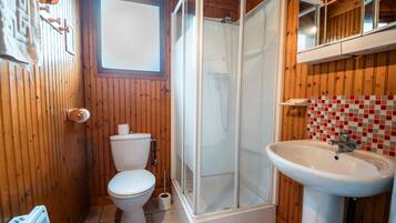 Ein Badezimmer mit Holzwandverkleidung, Toilette, einer Duschkabine und einem Waschbecken.
