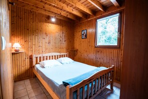 Un dormitorio de cabaña de madera con una cama, una ventana y un cuadro colgado en la pared.