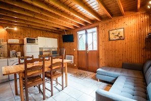 Ein Holzblockhaus-Interieur mit Esstisch, Stühlen, einer Couch, einem Fernseher und Küchengeräten.