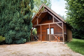 Une cabane en bois dotée d’un porche, entourée d’une forêt dense.