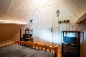 Ett sovrum med ett sluttande tak, en säng, en garderob och en skylt med texten ”HEM” på väggen.
