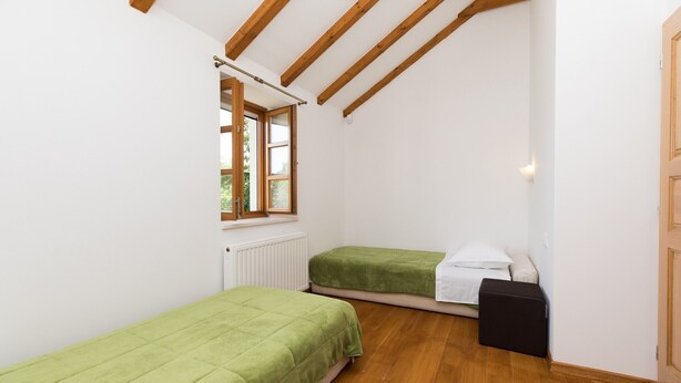 Een kleine, lichte kamer met houten balken, twee eenpersoonsbedden, een radiator en een raam.