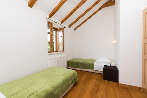 A small, bright room with wooden beams, two single beds, a radiator, and a window.