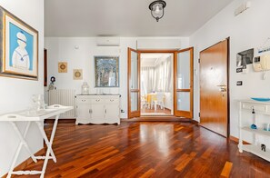 A room with a wooden floor, white furniture, a dining area with chairs and a table, and a door leading to another room. - ‘Sea View Suite Eventi Felici’ Apartment with Terrace, Sea View, Wi-Fi & Air Conditioning (Bari)