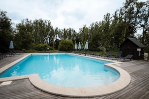 Une piscine rectangulaire avec une terrasse en bois, entourée de chaises longues et de parasols.