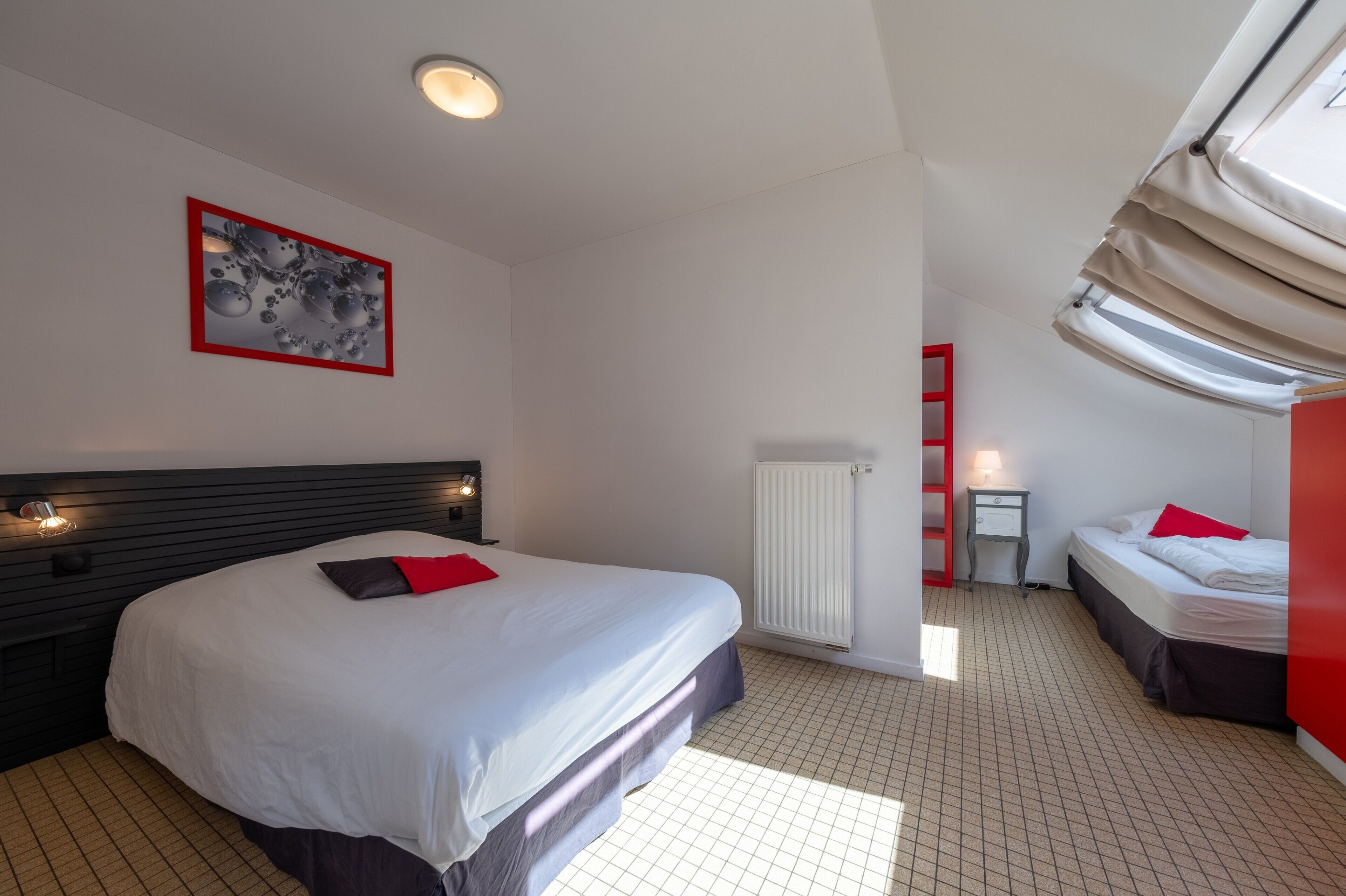 Une chambre d’hôtel avec un grand lit, une table de chevet, un radiateur, une fenêtre avec des rideaux et un tableau au mur.