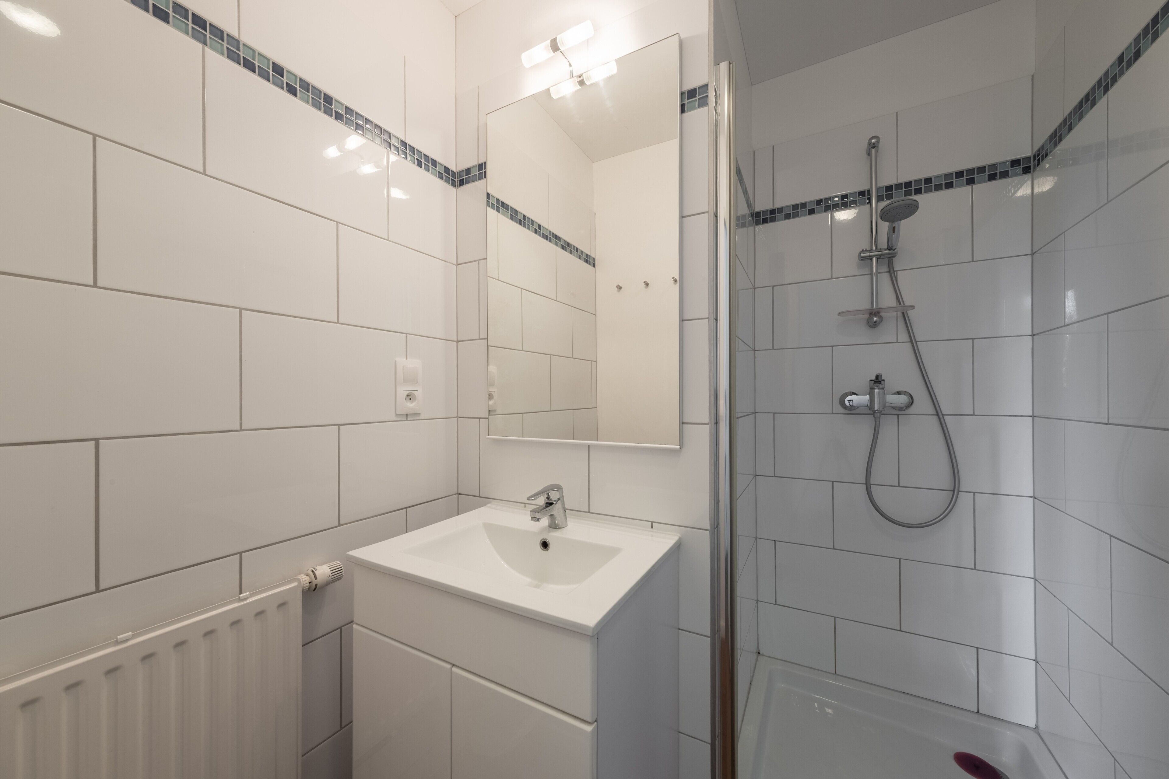 Un baño moderno con un lavamanos blanco, un espejo y una zona de ducha.