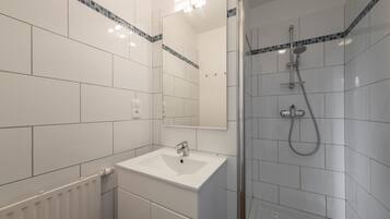 Un baño moderno con un lavamanos blanco, un espejo y una zona de ducha.