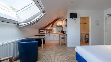 A room with a bed, a desk, a chair, a kitchenette, and a bathroom.