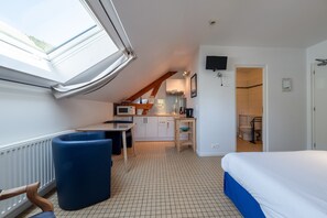A room with a bed, a desk, a chair, a kitchenette, and a bathroom.