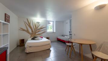 Une chambre moderne avec un lit, une petite table et une chaise. Il y a une fenêtre donnant sur des arbres.