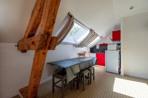 A compact kitchen with a dining area, a window with curtains, and a red cabinet.