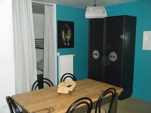 A dining area with a wooden table, black chairs, a woven chair, a black wardrobe, a white radiator, and a Buddha statue on the wall.