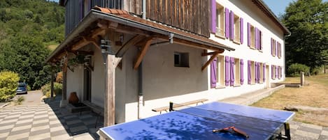 Un bâtiment à deux étages doté d’un sol extérieur à carreaux, d’une table de ping-pong et d’une voiture garée à proximité.