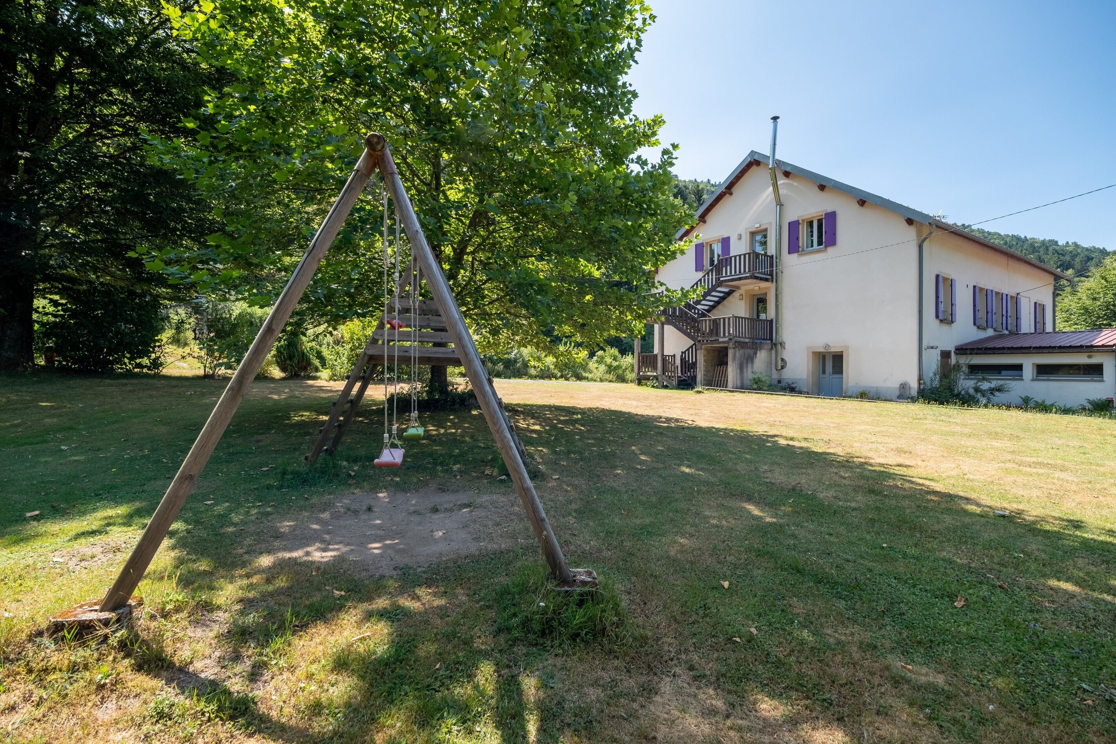 A wooden swing set in a grassy area with a building in the background.