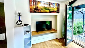 Een moderne woonkamer met een flatscreen televisie, een schilderij van een boslandschap en een waterpijp op een plank.