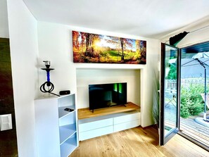 A modern living room with a flat-screen TV, a painting of a forest scene, and a hookah on a shelf. - Apartment 'Auszeit Im Grünen' with Shared Terrace, Private Garden and Wi-Fi (Greilitz)
