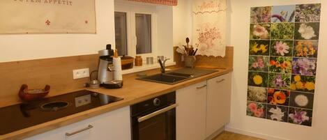 A kitchen with a wooden countertop, a coffee machine, a sink, and a wall-mounted oven.