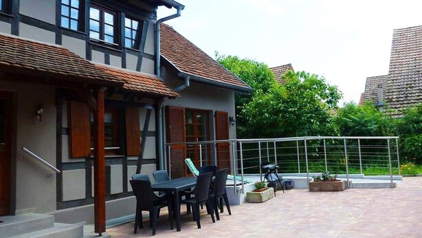 A two-story building with a balcony, outdoor seating, and potted plants. - Holiday Home “La Maison De Mediovilla” with Private Terrace, Garden & Wi-Fi (Wingersheim les Quatre Bans)