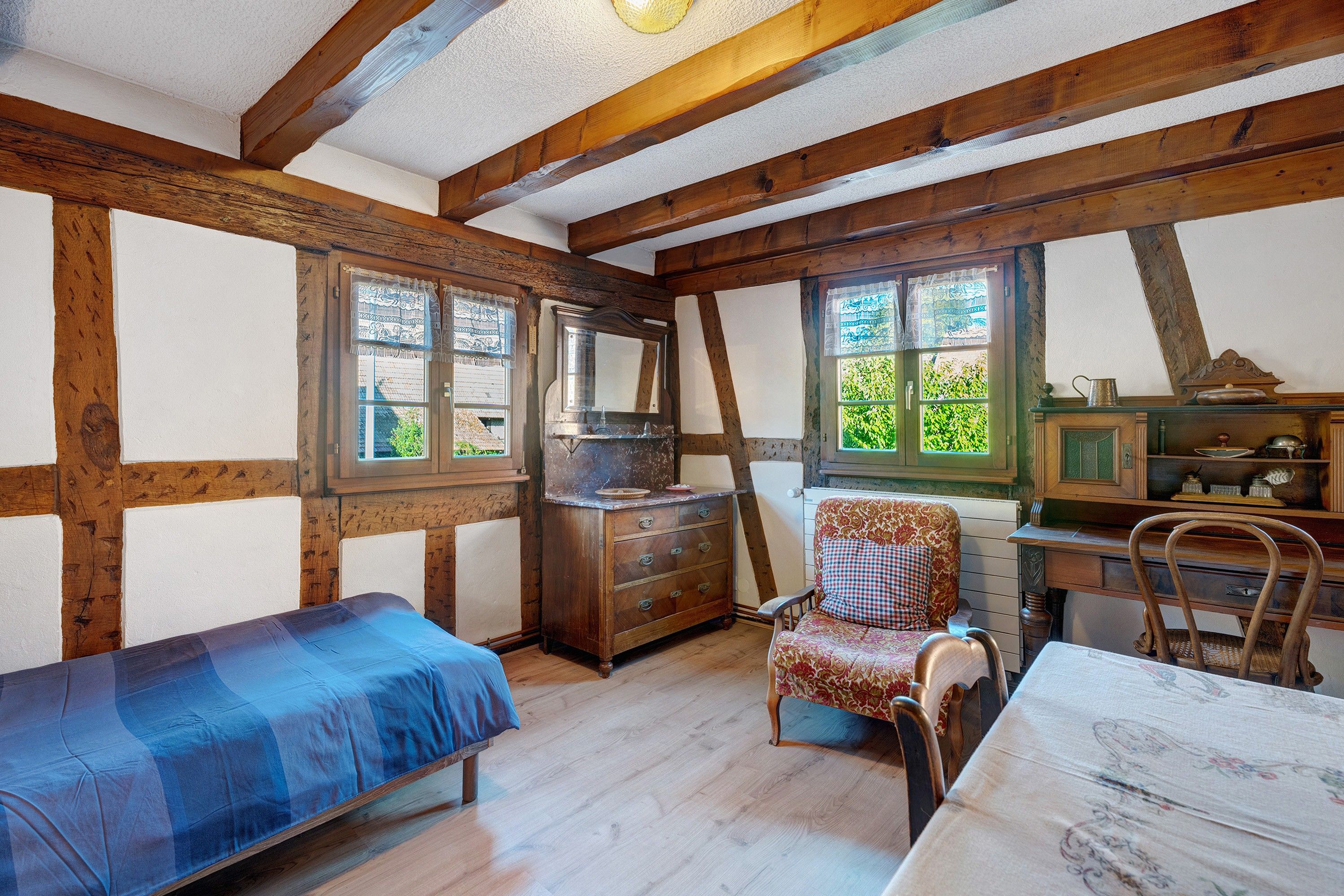 Een kamer met zichtbare houten balken, een bed, een stoel, een tafel en een dressoir.