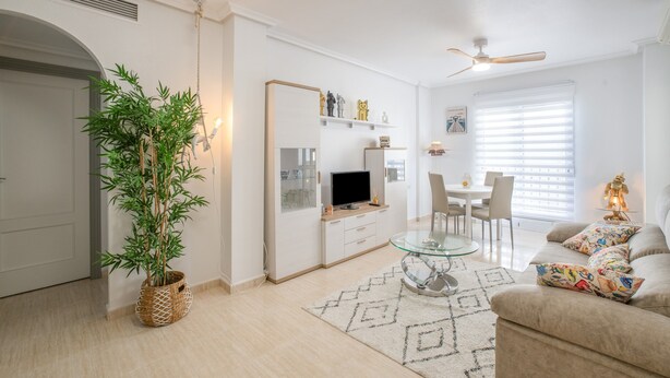 Un salon moderne avec un téléviseur à écran plat, une table à manger, un canapé, un ventilateur de plafond et une plante en pot.