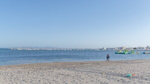 Une plage avec un ciel dégagé, un rivage sablonneux et des bateaux sur l’eau.