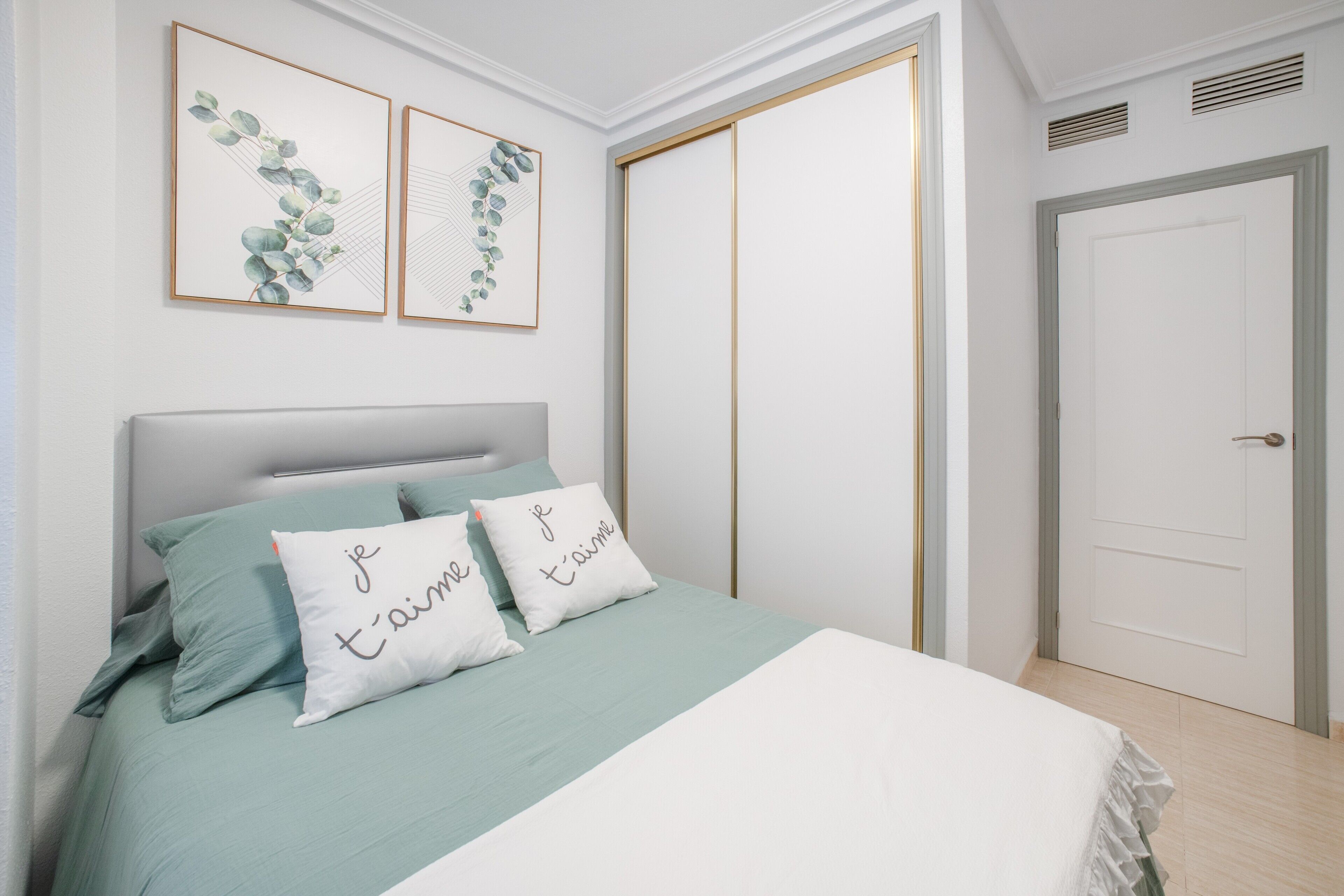 A bedroom with a bed, pillows, a wardrobe, and artwork on the wall.