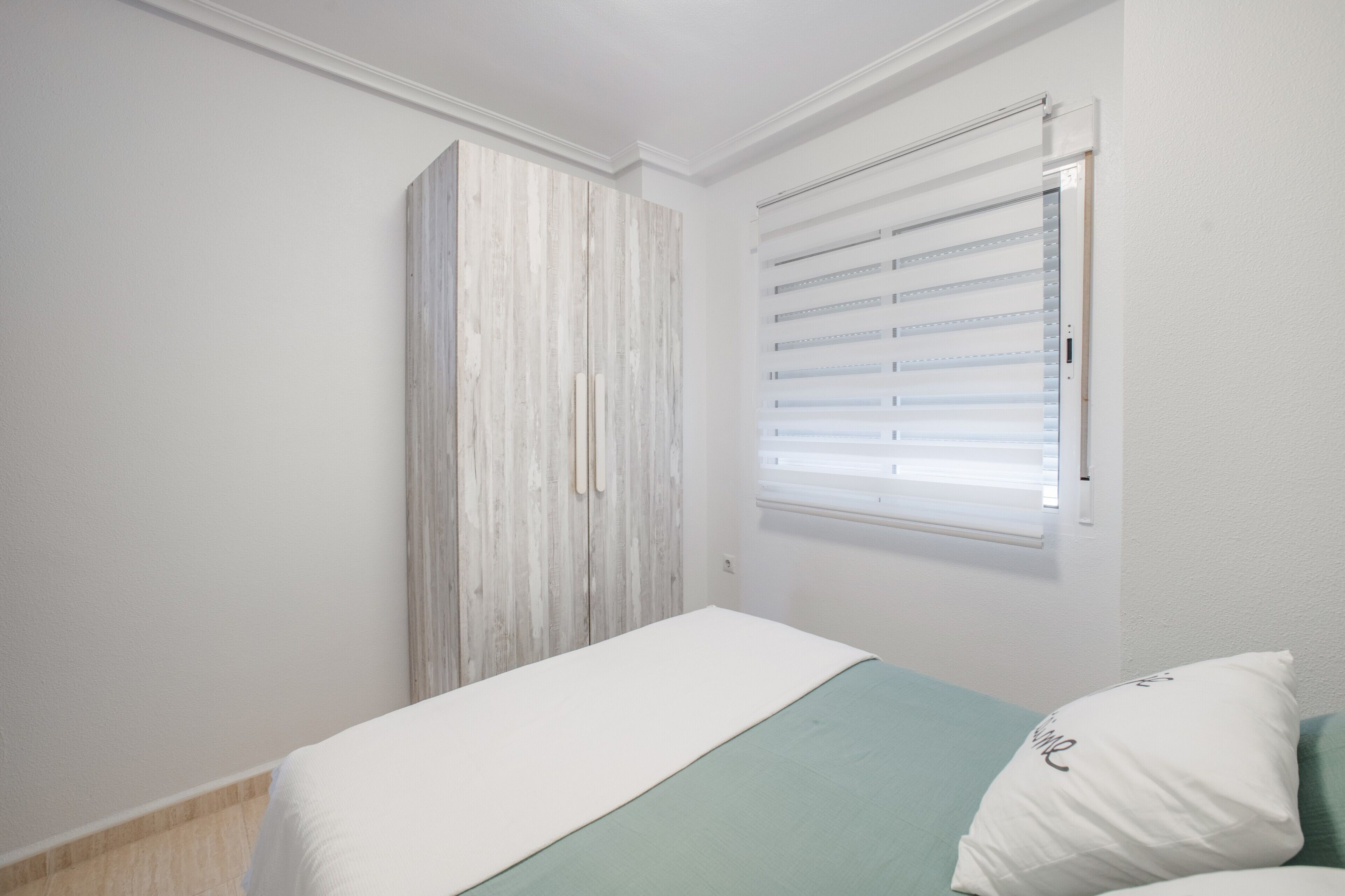 Ein Schlafzimmer mit Bett, Kleiderschrank und einem Fenster mit Jalousien.