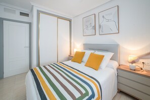 Ein Schlafzimmer mit einem Bett, zwei Nachttischlampen, einem Nachttisch, einer Tür und zwei gerahmten Kunstwerken an der Wand.