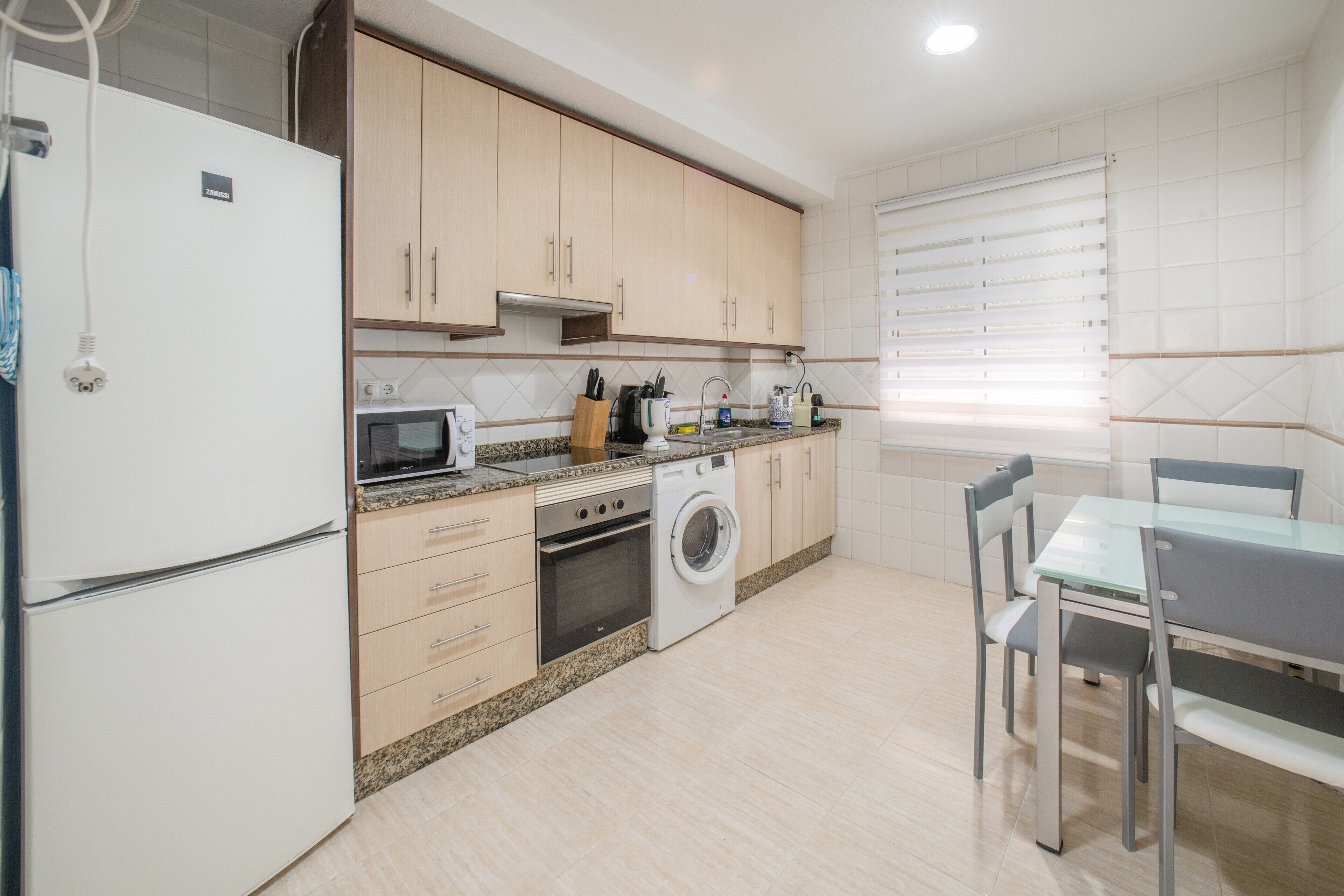 A modern kitchen with a refrigerator, microwave, oven, and washing machine.