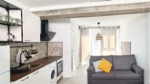 Un espace de vie compact comprenant un coin cuisine, un canapé gris et une grande fenêtre.