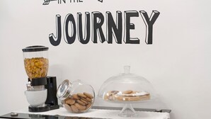 A breakfast setup with a cereal dispenser, a bowl of cookies, and a covered dessert display on a table against a wall with the text 'IN THE JOURNEY'. - Camera Mare - Casa Del Capitano, with Wi-Fi and Air Conditioning (Chioggia)