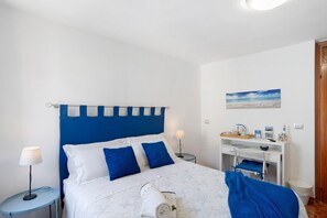 Ein Schlafzimmer mit einem Bett, einem Nachttisch, einem Schreibtisch und einem an der Wand befestigten Regal.