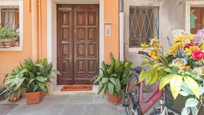A building entrance with a wooden door, numbered 805, potted plants, a bicycle, and a welcome mat. - Camera Mare - Casa Del Capitano, with Wi-Fi and Air Conditioning (Chioggia)