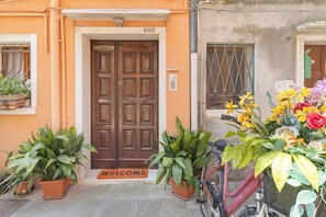 A building entrance with a wooden door, numbered 805, potted plants, a bicycle, and a welcome mat. - Camera Mare - Casa Del Capitano, with Wi-Fi and Air Conditioning (Chioggia)