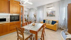 A modern kitchen with wooden cabinets, a dining table with chairs, a yellow sofa with patterned cushions, and a painting on the wall. - Camera Mare - Casa Del Capitano, with Wi-Fi and Air Conditioning (Chioggia)