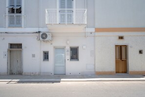 Un edificio con fachada blanca, un balcón con barandilla blanca y una puerta con ventanal.