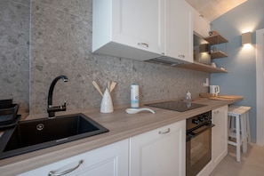 Una cocina con un lavamanos negro, armarios blancos, encimera de madera, horno empotrado y estante con utensilios de cocina.